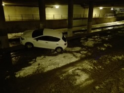 Белый автомобиль стоит на грязной поверхности под мостом